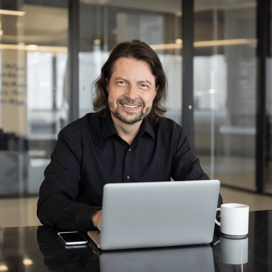 AVGS-Coaching Unternehmensberatung Fördermöglichkeiten nutzen trust-plan-genial.de 1 Maik Marx von plangenial.de im schwarzen Hemd am Laptop im modernen Büro – konzentriert bei der Arbeit.